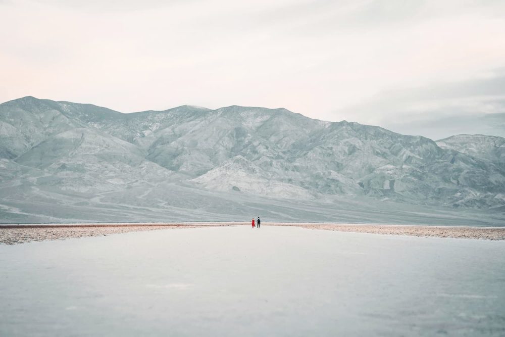 Lonely couple walking Badwater Basin Salt Flat Trail under the imposing heights of the Panamint Range