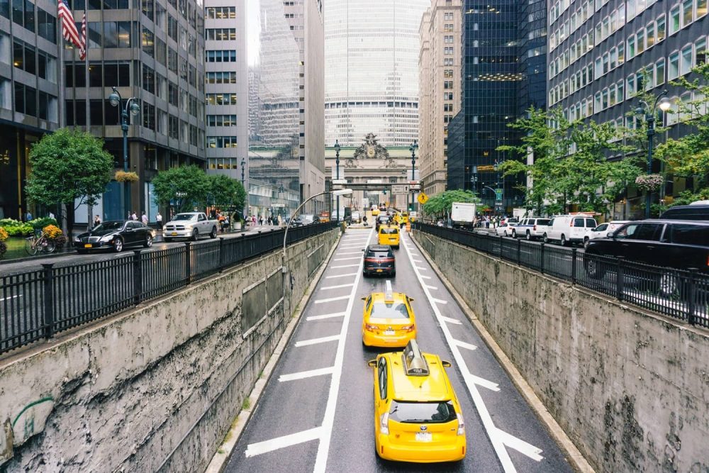 Yellow cabs on a busy street flanked by towering skyscrapers in NYC