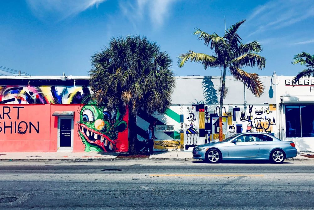 Car parked in front of vivid murals depicting strange characters in Wynwood, Miami