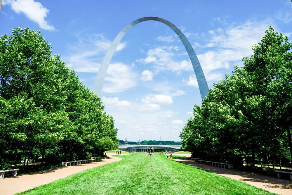 People crossing the green lawns under the rising Gateway Arch in St. Louis